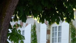 A building with white shutters, ivy-covered walls, and a small patio with two white chairs and a table. - La Tonnellerie (Tavers)