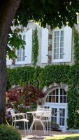 Un bâtiment aux volets blancs, aux murs recouverts de lierre et doté d’un petit patio avec deux chaises blanches et une table.
