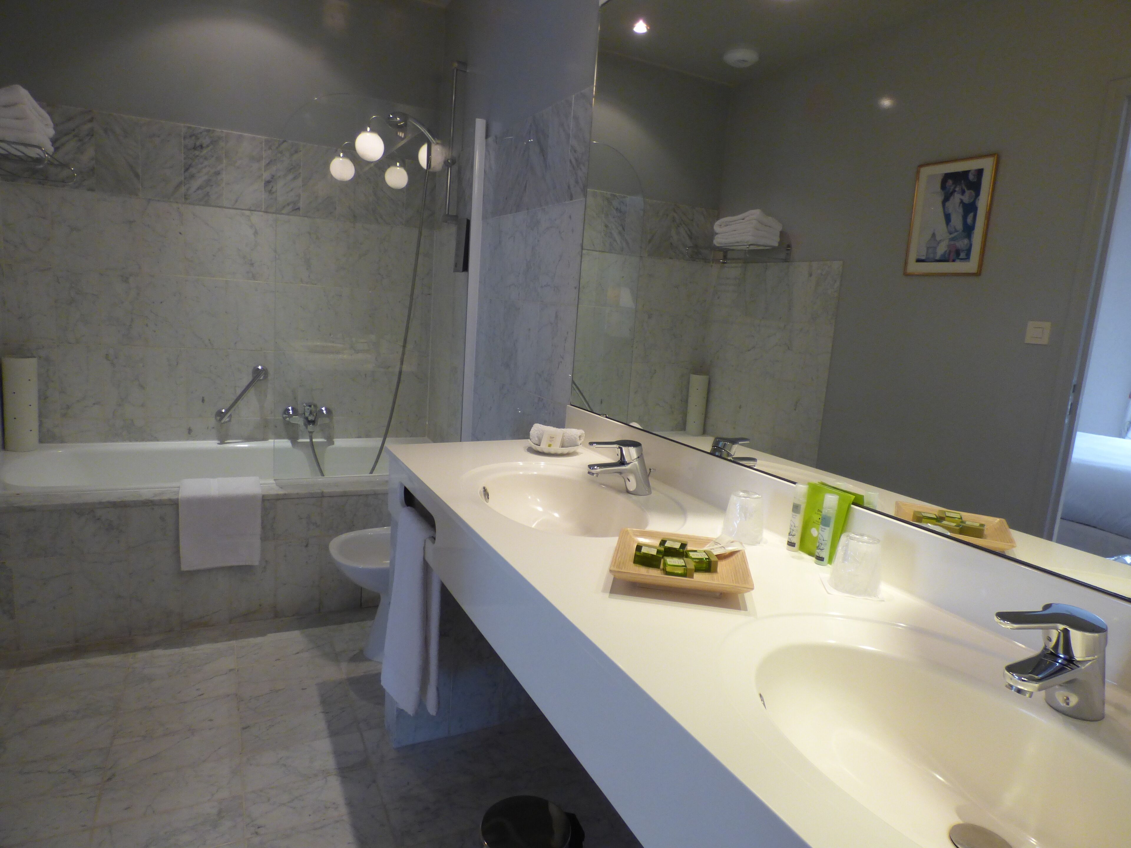 Een moderne badkamer met een grote spiegel, twee wastafels, een bad en een douche.