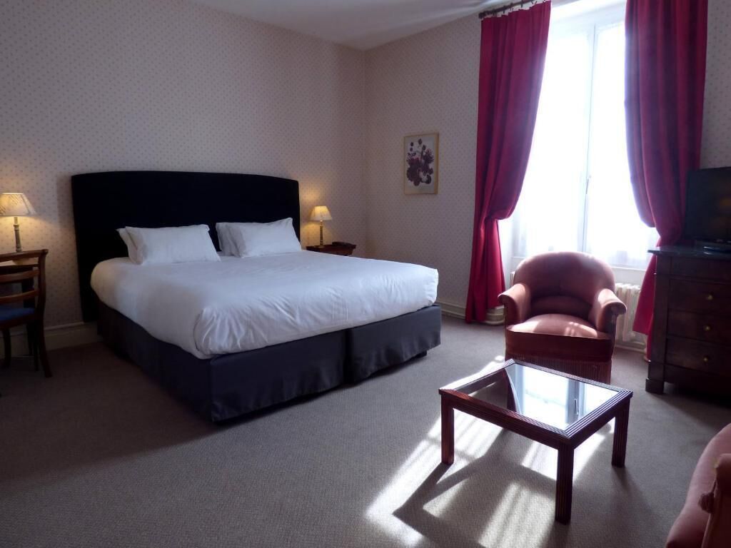 A hotel room with a large bed, a wooden nightstand, a glass coffee table, a red armchair, and a television.