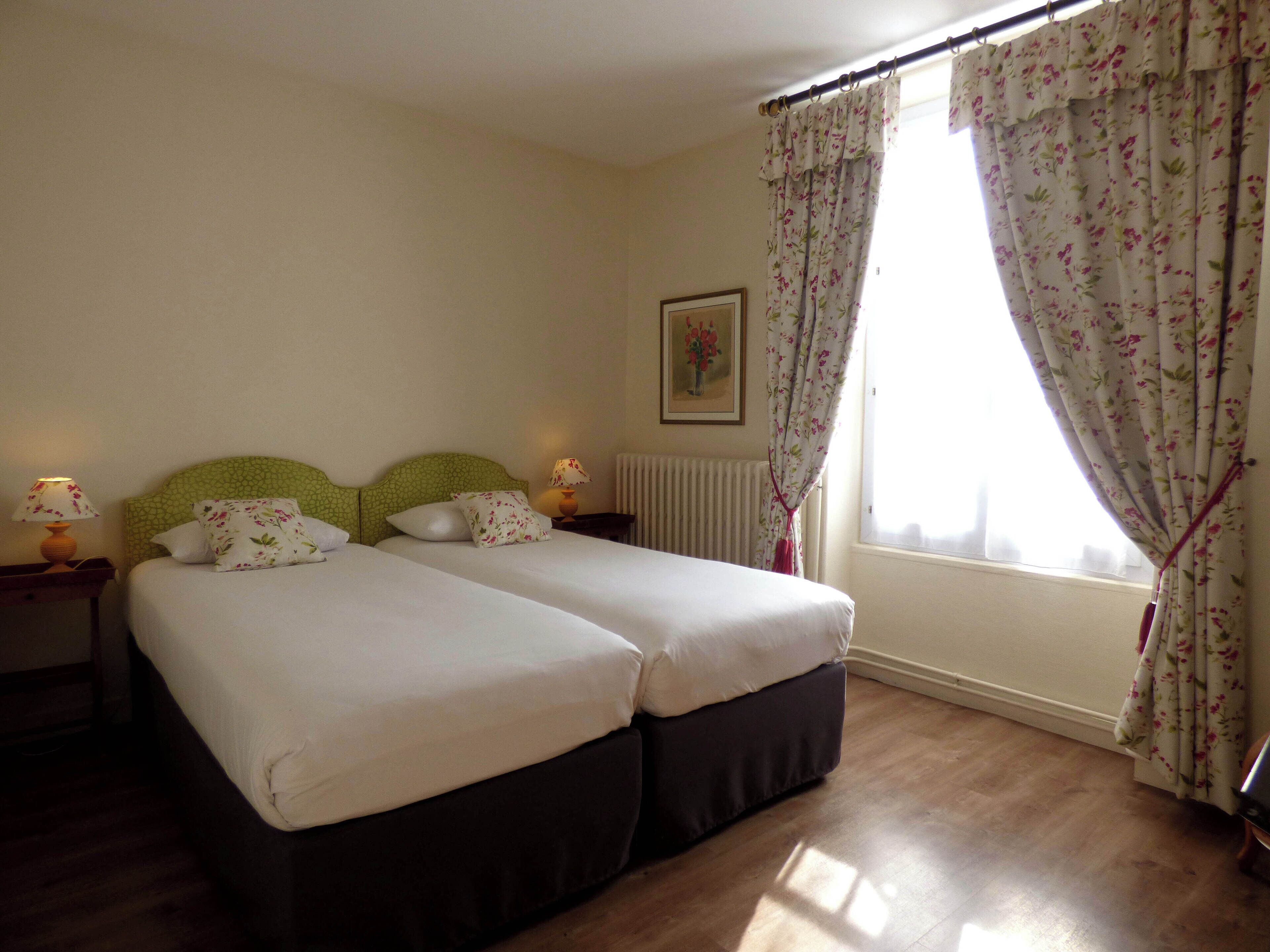 A double room with two beds, a radiator, a framed picture on the wall, and a window with floral curtains.