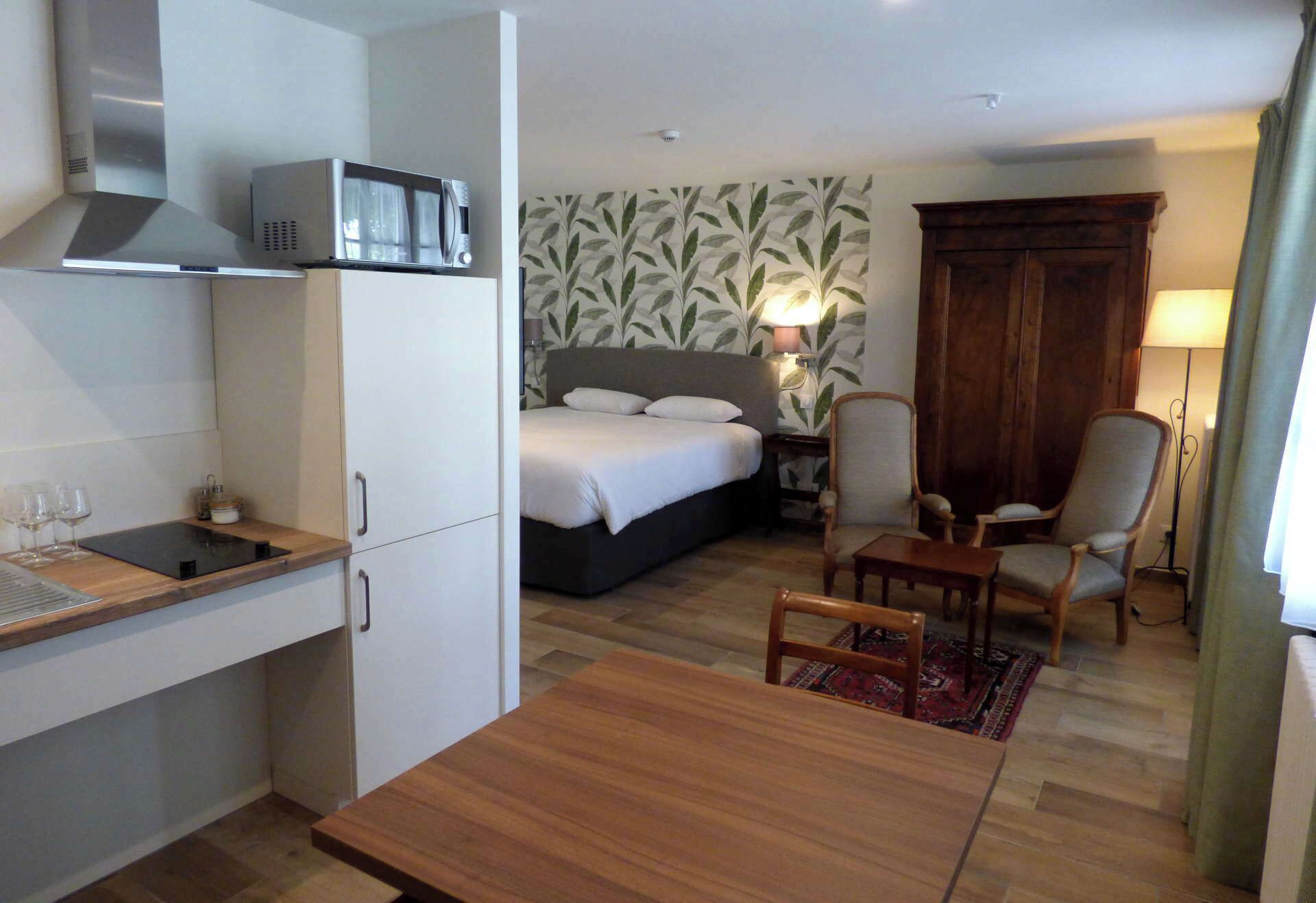 Una habitación de hotel compacta con kitchenette, una cama, un escritorio y una silla.