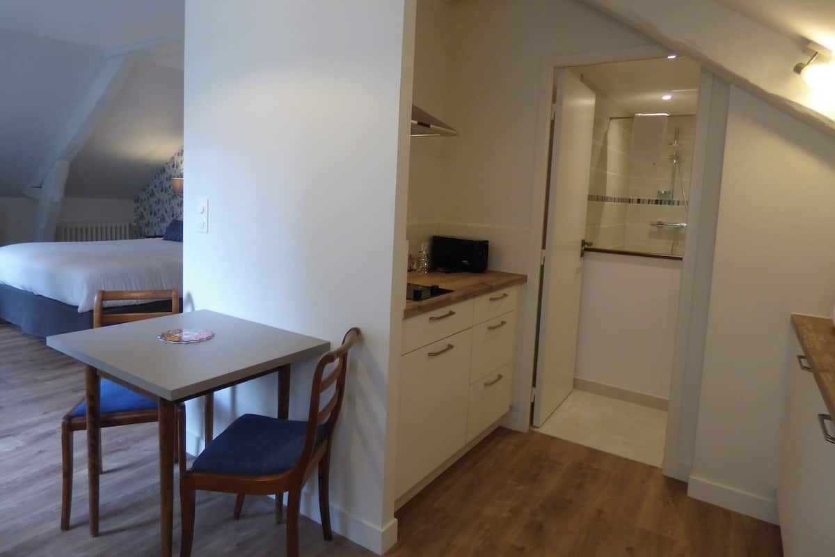 A bedroom with a bed, a small table with a chair, and a kitchenette with a microwave.