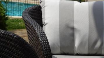 A wicker chair with a striped cushion, a pool in the background, and a grassy area.