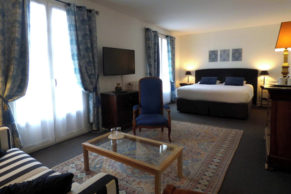 A hotel room with a bed, a chair, a TV, a desk, and a coffee table.