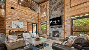 A spacious living room with a stone fireplace, wooden walls, and a mounted television.