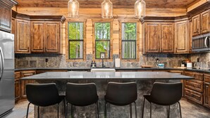 A kitchen with wooden cabinets, a large island with bar stools, and a stone backsplash.