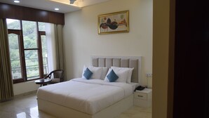 A spacious bedroom with a large bed, a nightstand, a chair, and a window with curtains. - Xenious Micro Dharmshala  (Dharamshala)