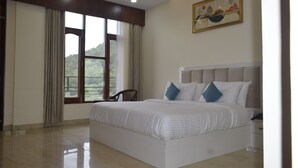 A spacious bedroom with a large bed, a chair, a nightstand, and a window with curtains. - Xenious Micro Dharmshala  (Dharamshala)