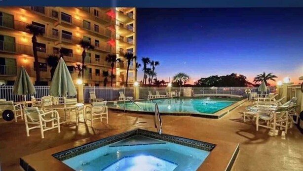 A pool area with multiple hot tubs and lounge chairs, surrounded by a fence and palm trees. - Salt Life Escape: 2B/2B in Oceanfront Complex (Cocoa Beach)