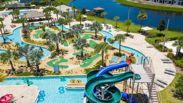 Un parque acuático con una piscina grande, varias toboganes y una zona de campo de golf.