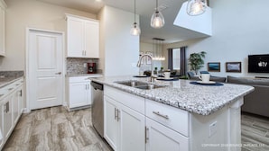 Una cocina moderna con encimeras de granito, armarios blancos e iluminación colgante.