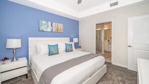 Un dormitorio con una cama, dos mesitas de noche, un ventilador de techo y una puerta al baño.