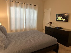 A bedroom with a bed, a dresser, a TV on the wall, and a window with curtains. - 4bed Home in Storey Lake With Private Pool (Kissimmee)