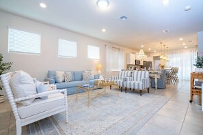 A spacious living room with a sofa, armchairs, a coffee table, and a dining area with a chandelier. - Amazing 5 Suite Home With Resort-style Amenities (Davenport)