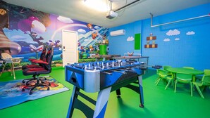 A room with a foosball table, green chairs, and a colorful mural. - Amazing 5 Suite Home With Resort-style Amenities (Davenport)