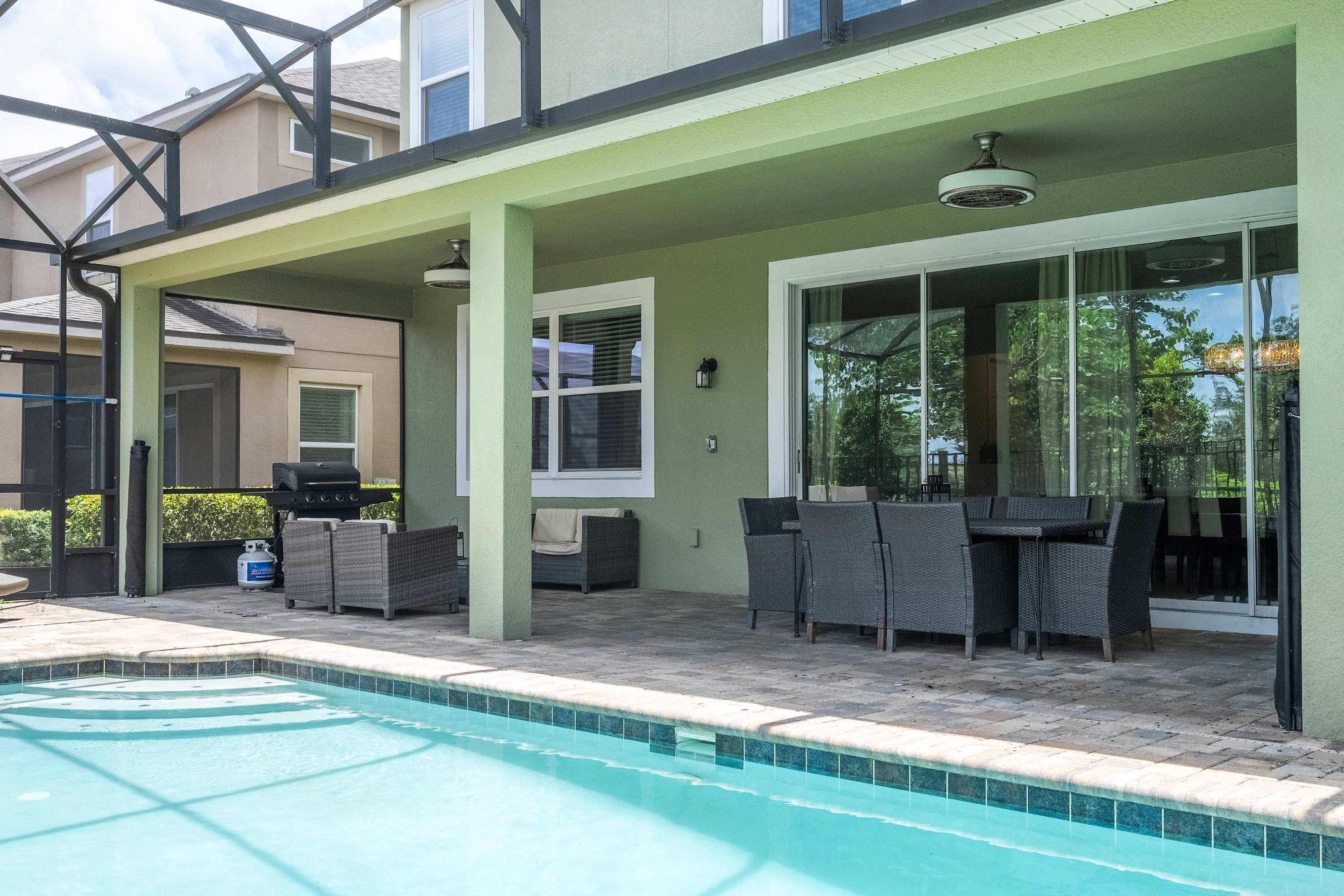 A poolside area with a covered patio, outdoor furniture, and a barbecue grill.