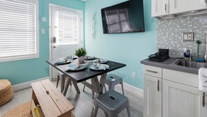 A kitchen with a teal wall, white cabinets, a wooden table with plates, and a bench. - Cozy 1BR condo North Wildwood with WiFi, AC, 1.5 blk to beach, Boardwalk, Moreys (North Wildwood)