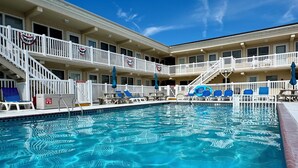 A swimming pool with clear blue water, surrounded by a white fence and blue lounge chairs. - Cozy 1BR condo North Wildwood with WiFi, AC, 1.5 blk to beach, Boardwalk, Moreys (North Wildwood)