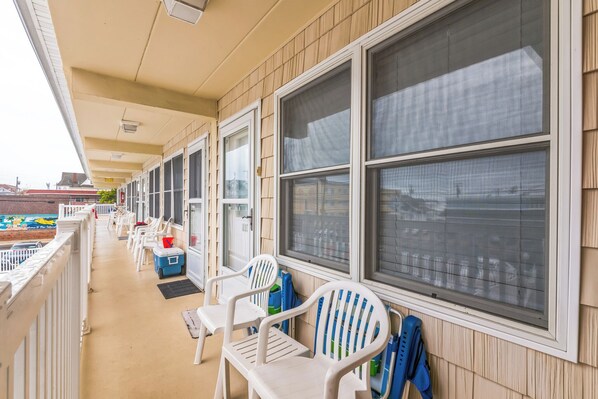 A row of rooms with large windows, a covered outdoor area with chairs and a cooler, and a view of the cityscape.