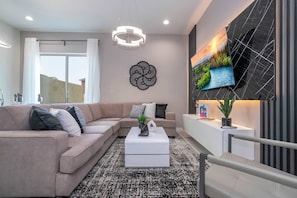 A modern living room with a beige sectional sofa, a white coffee table, and a large flat-screen TV mounted on a black wall.