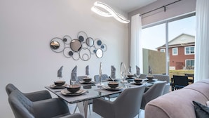 Ein moderner Essbereich mit einem Glastisch, grauen Stühlen und einer wandmontierten Spiegel-Kunstinstallation.