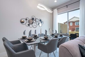 Ein moderner Essbereich mit einem Glastisch, grauen Stühlen und einer wandmontierten Spiegel-Kunstinstallation.
