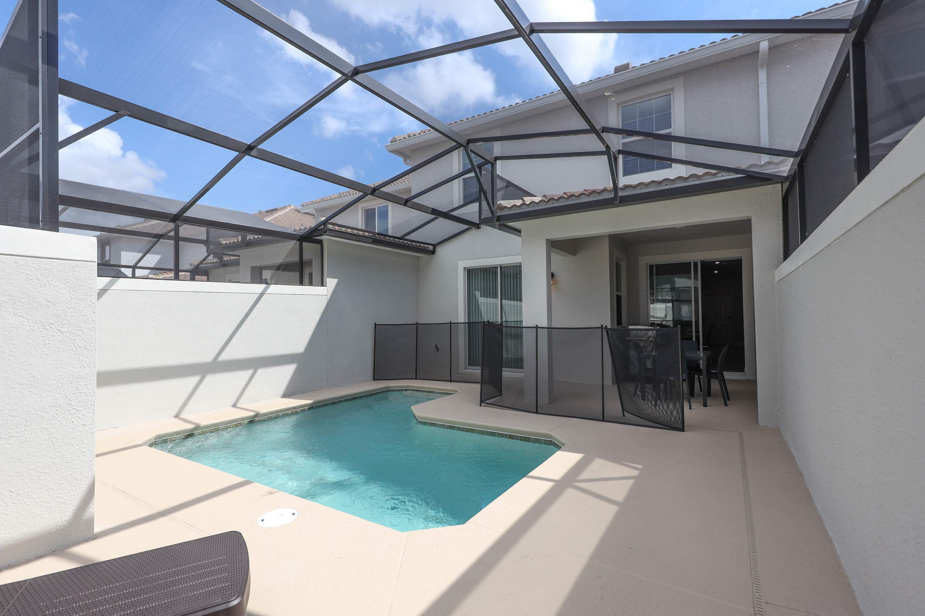 Une piscine dotée d’une structure en verre, entourée d’un mur blanc et d’une clôture métallique.