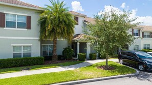 A residential building with a covered entryway, a palm tree, and a vehicle parked in the driveway.