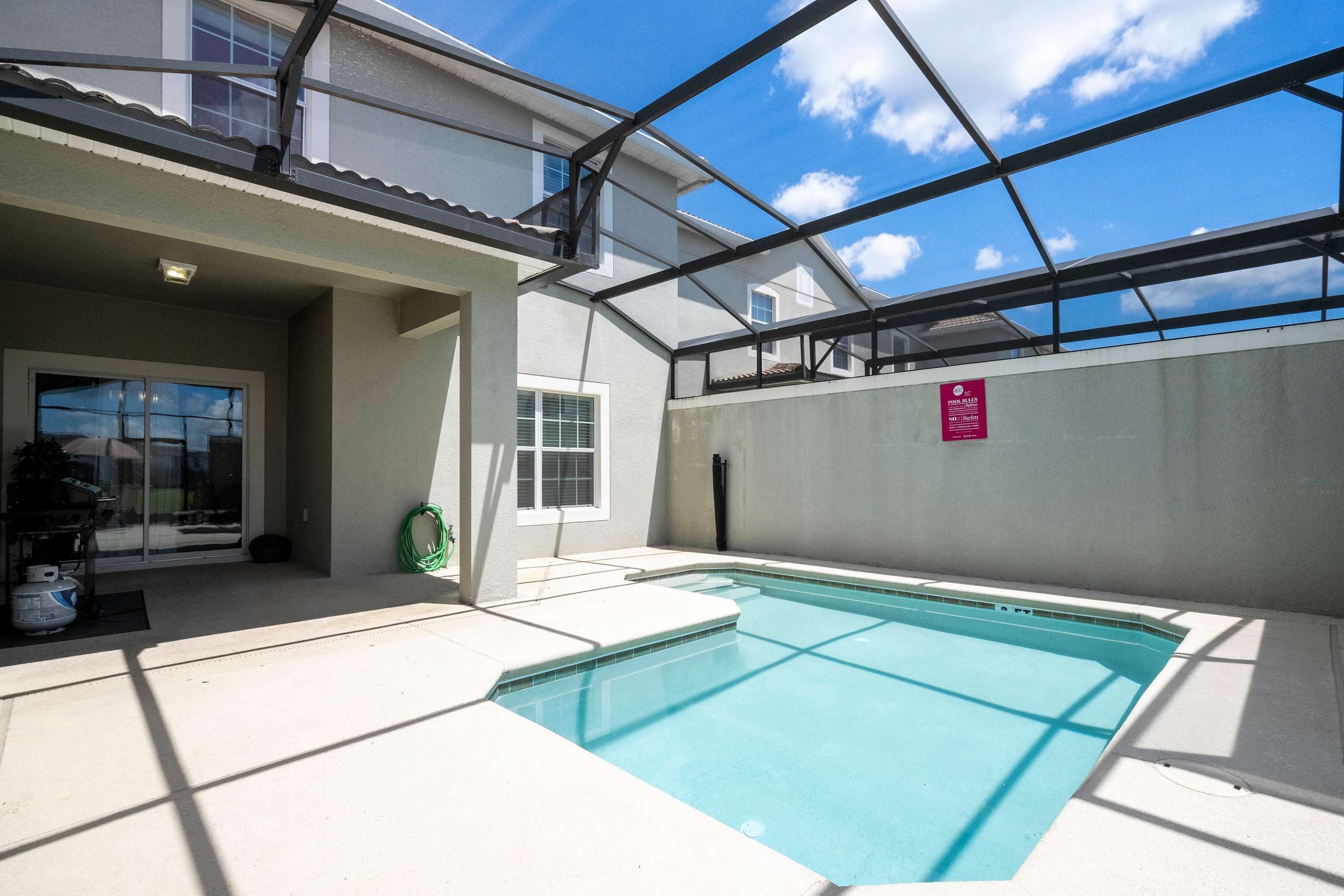 A swimming pool with a glass ceiling, a covered patio, and a clear blue sky.