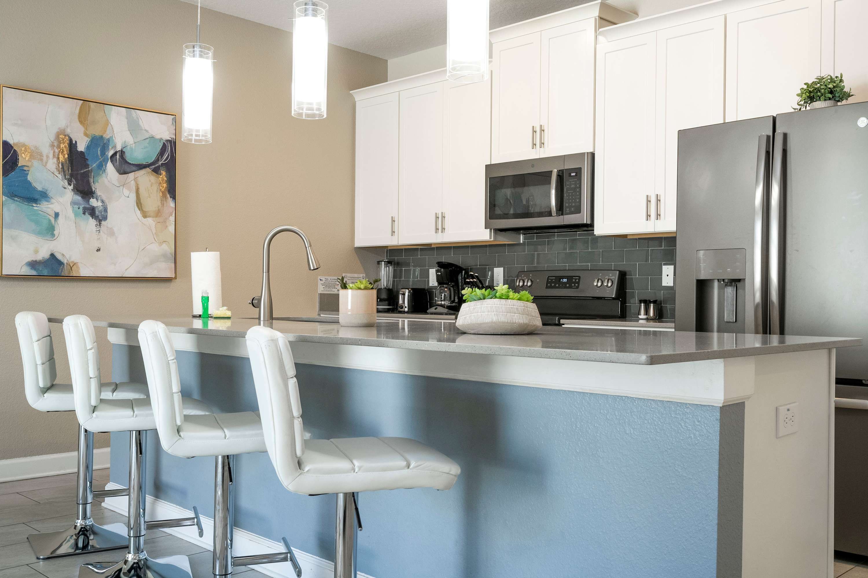 A modern kitchen with white cabinets, stainless steel appliances, a large island with bar stools, and a hanging light fixture.