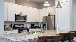 A modern kitchen with white cabinets, stainless steel appliances, granite countertops, and bar stools. - Modern Chic Home Mickey and Toy Story Rooms (Kissimmee)