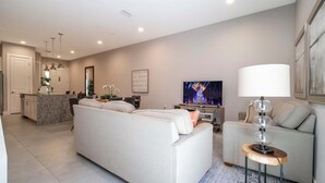 A modern living room with a sofa, a coffee table, and a TV. There is a kitchen area with a countertop and cabinets. - Modern Chic Home Mickey and Toy Story Rooms (Kissimmee)