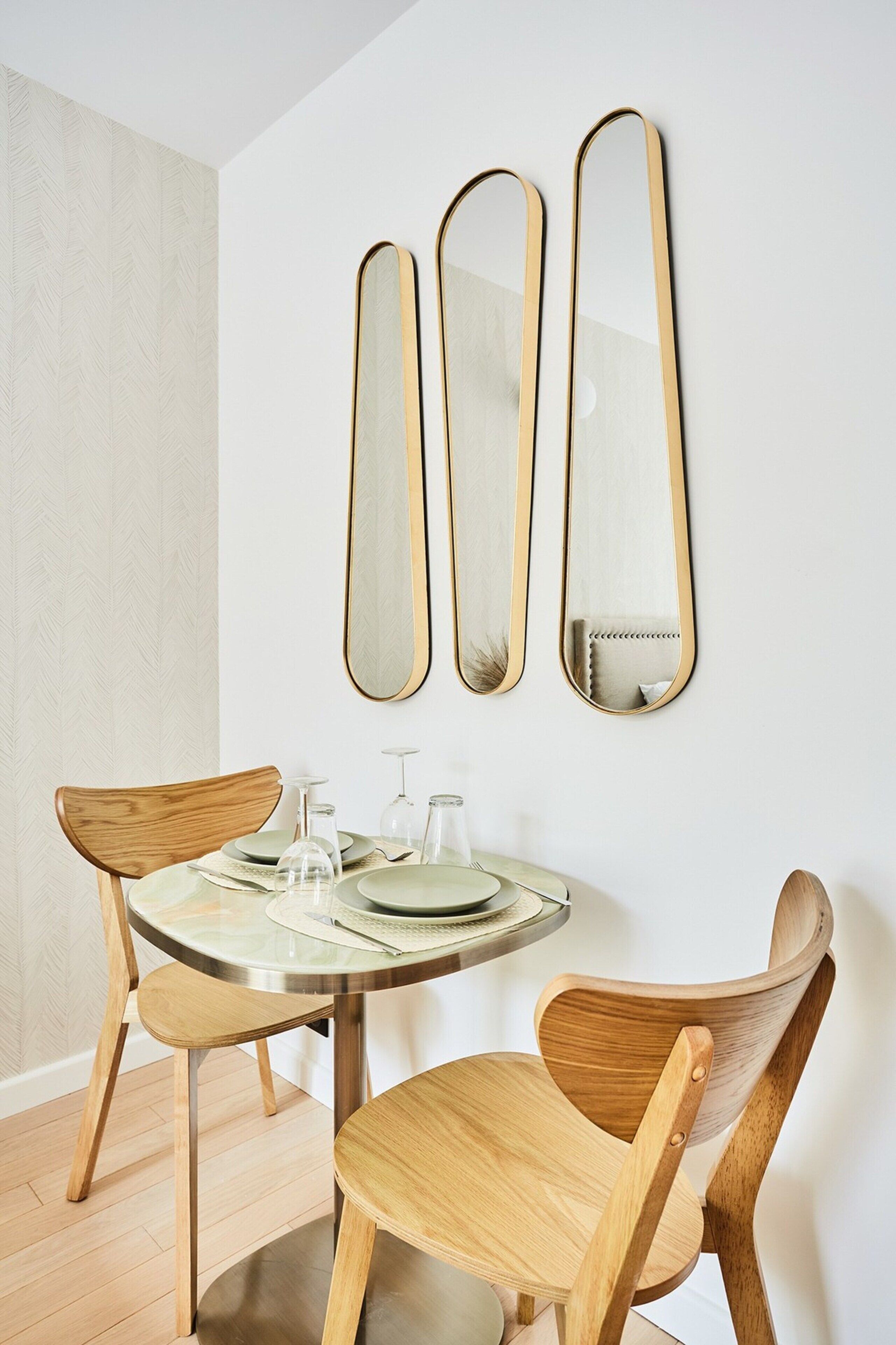 Un comedor con una mesa redonda, dos sillas de madera y tres espejos colgados en la pared.
