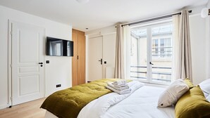 A hotel room with a bed, a television, a sliding door to a balcony, and a window with curtains. - Chic Studio AC - Center of Paris-bourse (Paris)