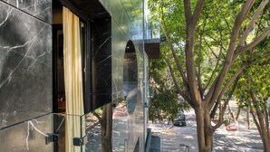 Un edificio moderno con entrada de vidrio, una calle bordeada de árboles y un coche estacionado.