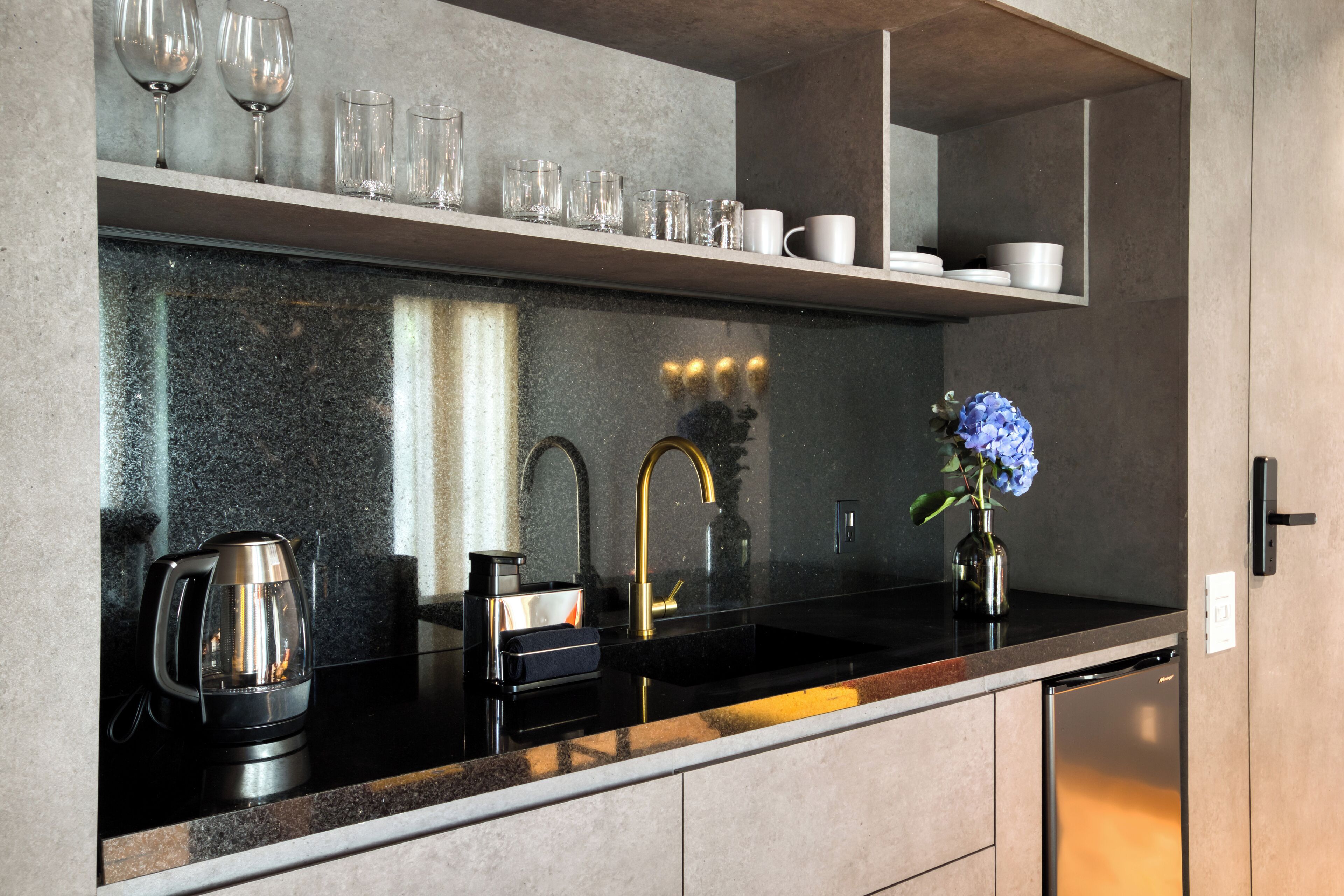 Eine moderne Küche mit schwarzem Arbeitsplatz, einem goldfarbenen Wasserhahn, einer Kaffeemaschine und einer Vase mit Blumen.