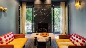 Una sala de estar moderna con chimenea, dos sofás con pompones rojos, una mesa de centro y vistas a árboles a través de amplios ventanales.