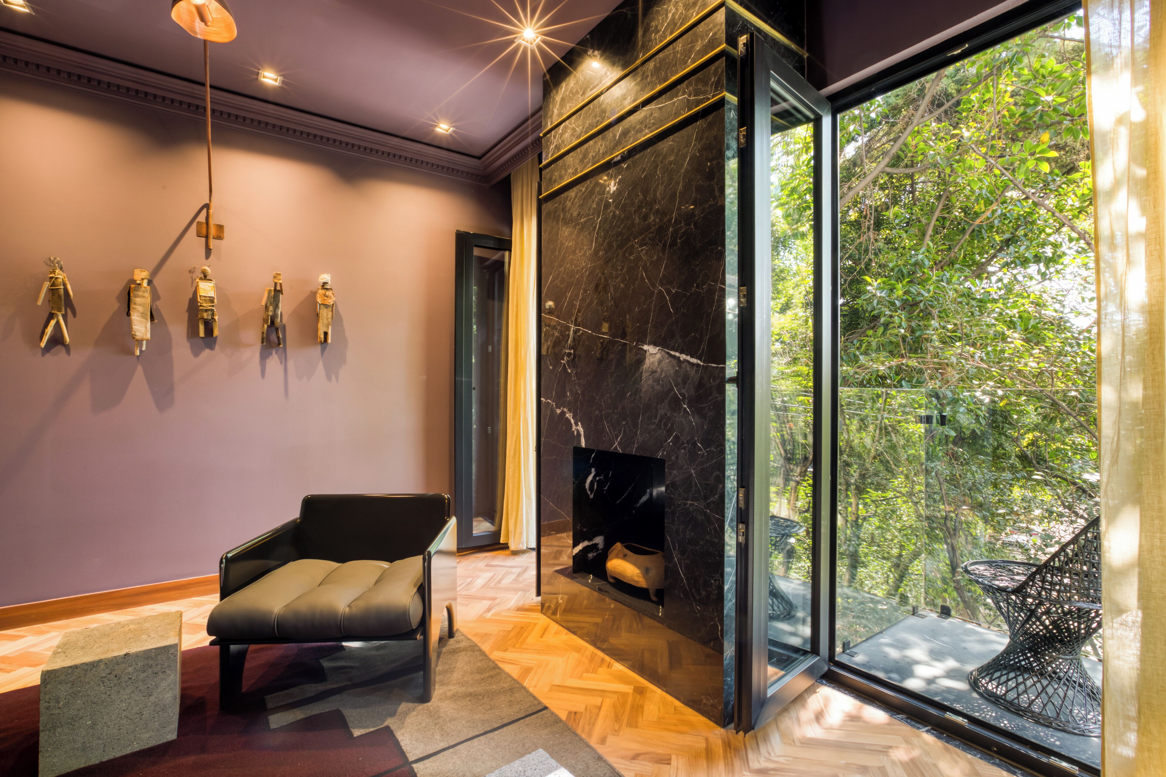 A modern interior with a fireplace, a sofa, and a view of greenery through large windows.