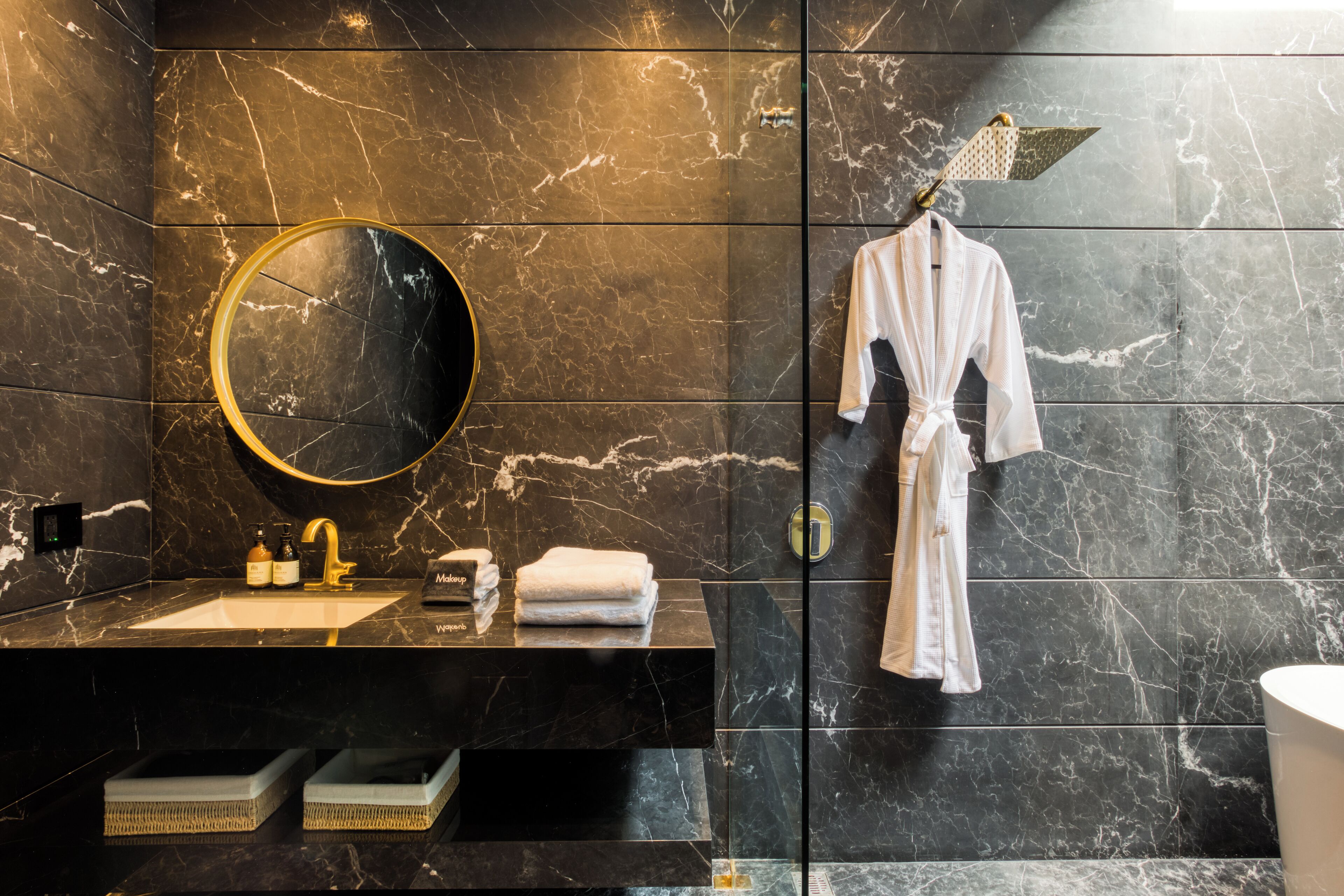 A modern bathroom with a marble sink, a round mirror, a robe hanging on the wall, and a shower with a unique showerhead.