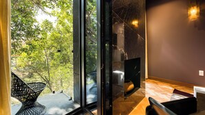 Un interior moderno con un gran ventanal que da a un espacio exterior, una silla de metal negro y una pared de mármol con una lámpara.