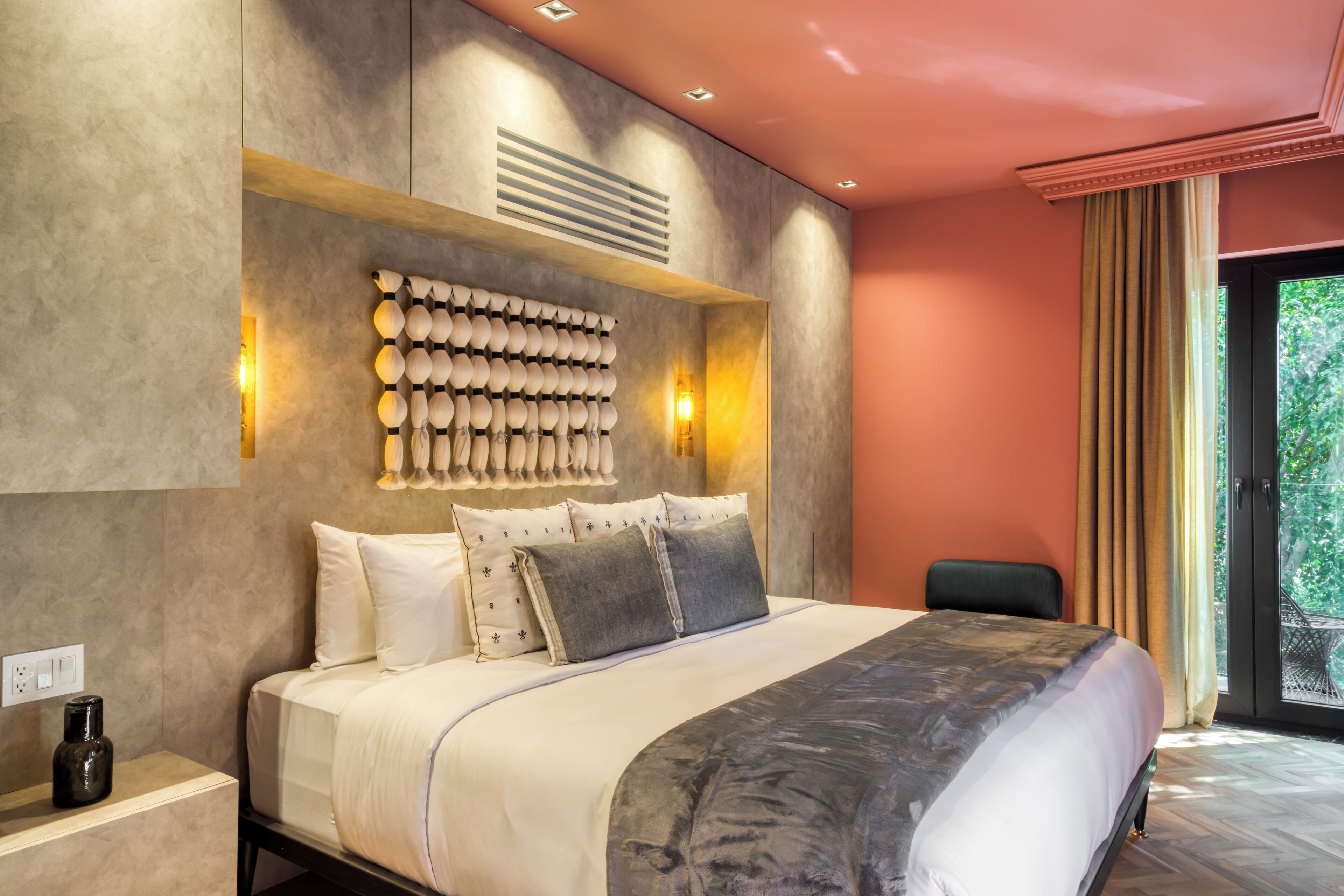 A modern bedroom with a large bed, a wall-mounted light fixture, and a window with curtains.