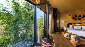 Habitación de hotel moderna con un ventanal grande, una cama con múltiples almohadas y un perchero para toallas en la pared.
