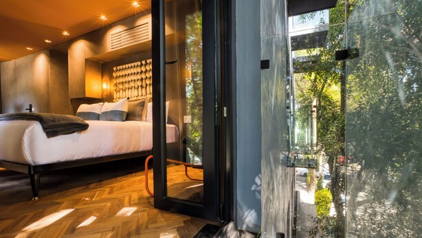 Un dormitorio moderno con una cama grande, una puerta de cristal que da a un balcón y un suelo de madera con diseño en espiga.