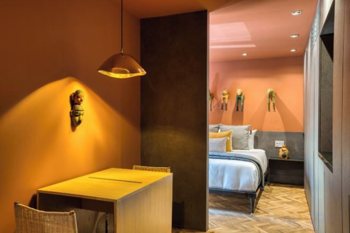 A hotel room with a bed, a desk, and a chair. There is a wall-mounted light fixture and a window.