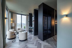 A modern hotel room with a large window, a seating area with a round table, and a black accent wall. - Panoramic Penthouse Apartment in Battersea (London)