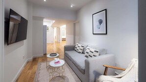 Una sala de estar moderna con un sofá gris, un sillón blanco y una pequeña mesa redonda con un objeto rosa.