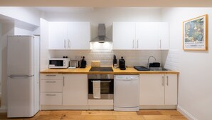 Cocina compacta con armarios blancos, microondas, tostadora, fregadero y lavavajillas.