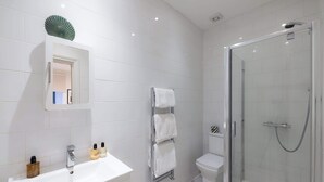Un baño moderno con lavamanos blanco, espejo y cabina de ducha de vidrio.