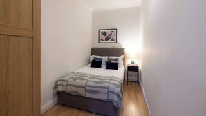 Un dormitorio con una cama, una mesita de noche, un cuadro enmarco y una puerta de madera.